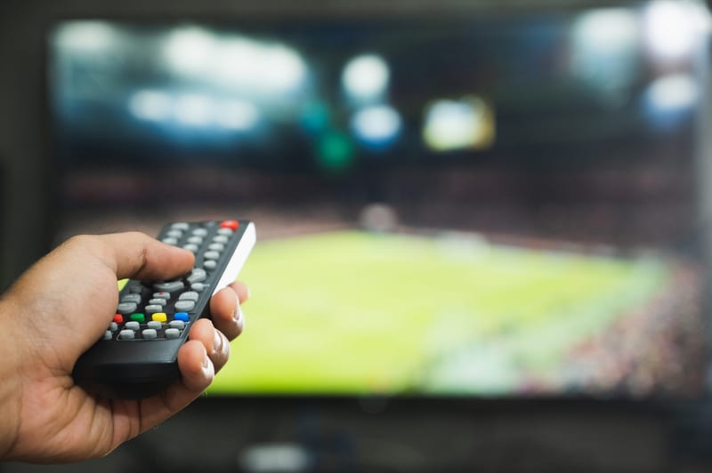 young man holding television remote control watching football pr